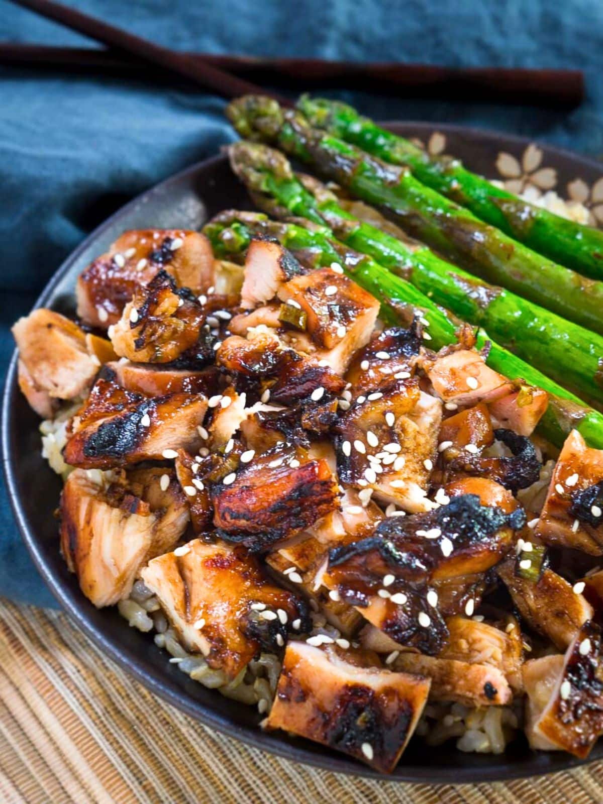 Angled view of grilled teriyake chicken and asparagus over rice and garnished with sesame seeds - Hostess At Heart