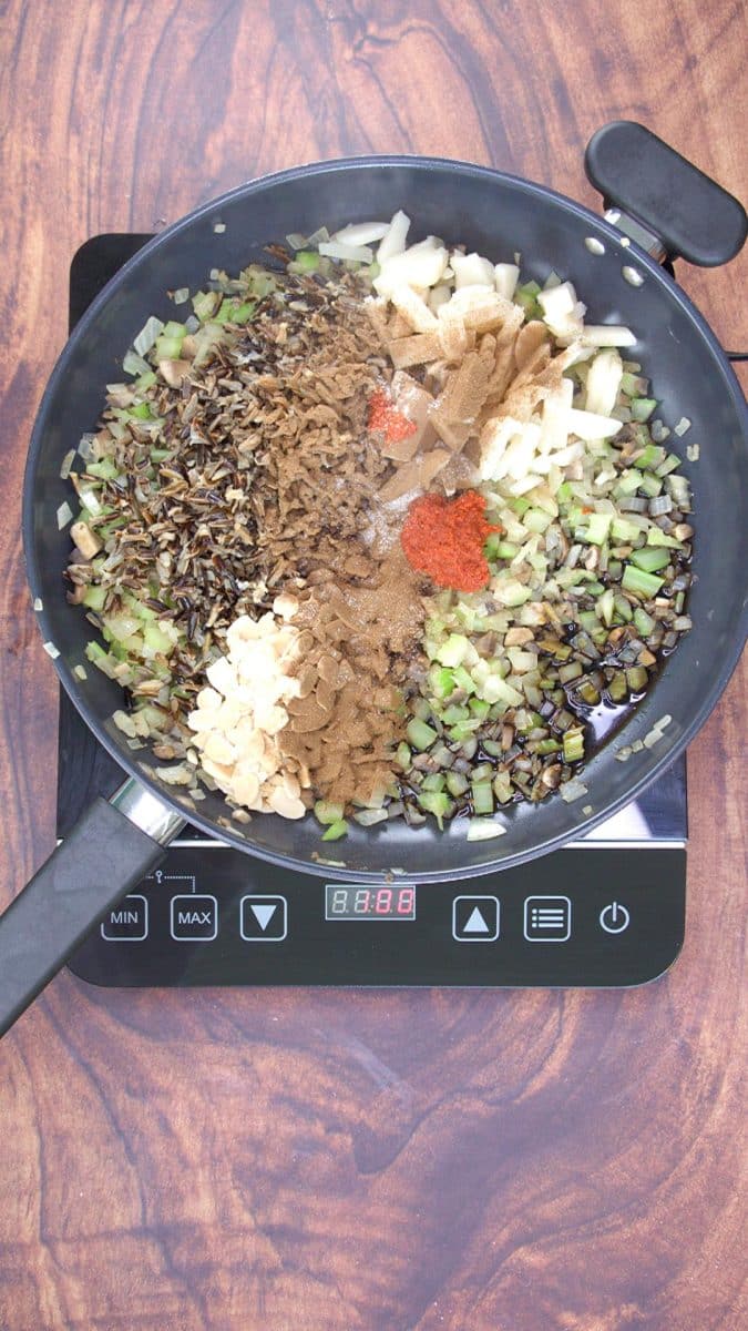 Top down view of a skillet containing cooked wild rice, chopped celery, mushrooms, chestnuts, and onions, that have been topped with chinese five spice powder, soy sauce, and curry paste. Hostess At Heart