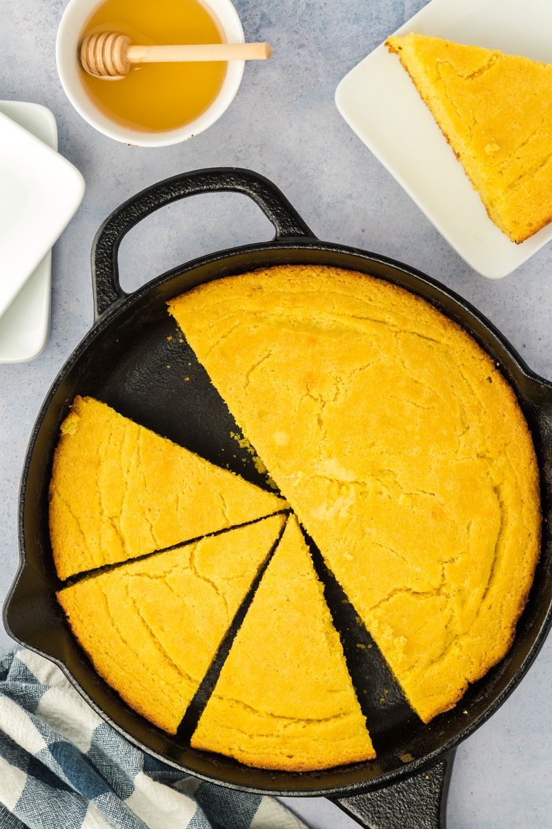 A cast iron skillet filled with baked cornbread that's been cut into wedges - Hostess at Heart