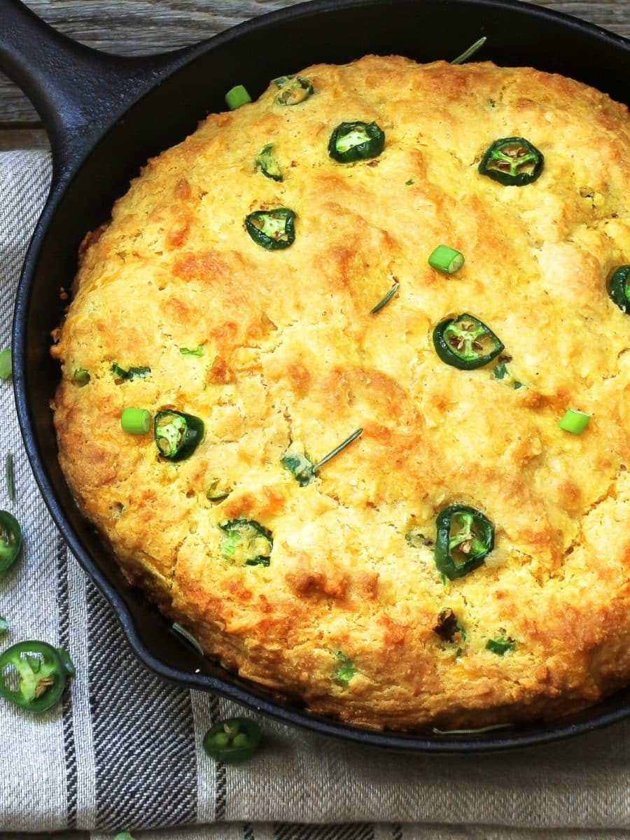 A cast iron skillet containing a baked cornbread filled with jalapenos