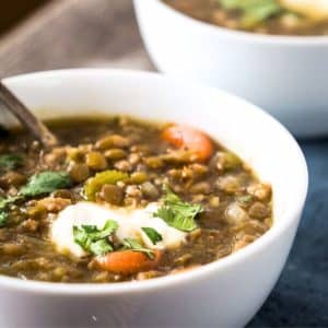 Angled view of lentil sausage soup with vegetables and a garnish of yogurt and cilantro. Hostess At Heart