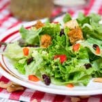 A sideview of a crispy green salad with sweet poppyseed dressing topped with croutons, fruit, and nuts. Hostess At Heart