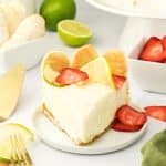 Front view of a slice of lime cheesecake with a graham cracker crust topped with slices of fresh strawberries and lime wheels. Hostess At Heart