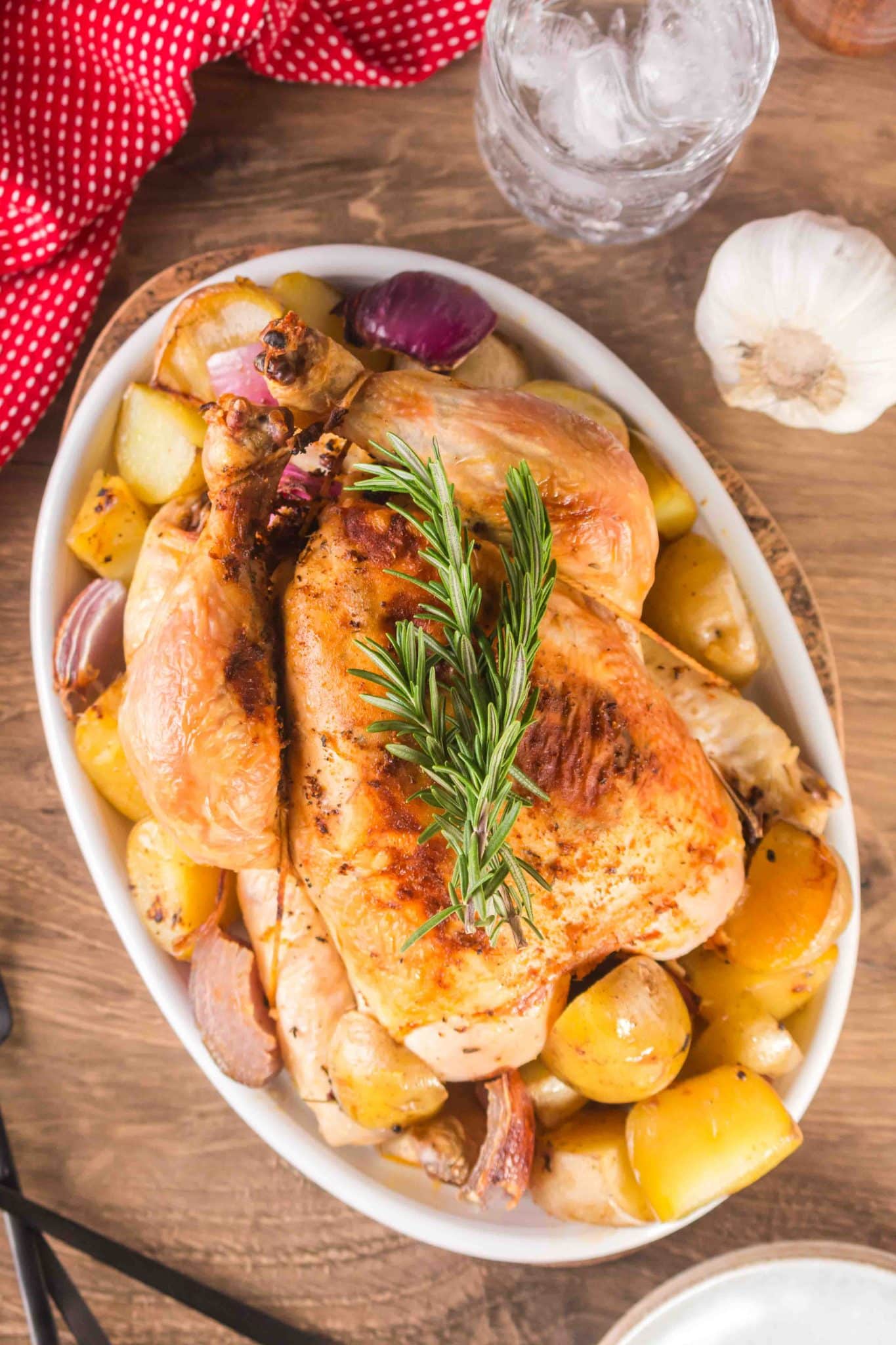 Whole chicken, top down view, resting in a baking dish surrounded by potatoes and onions.