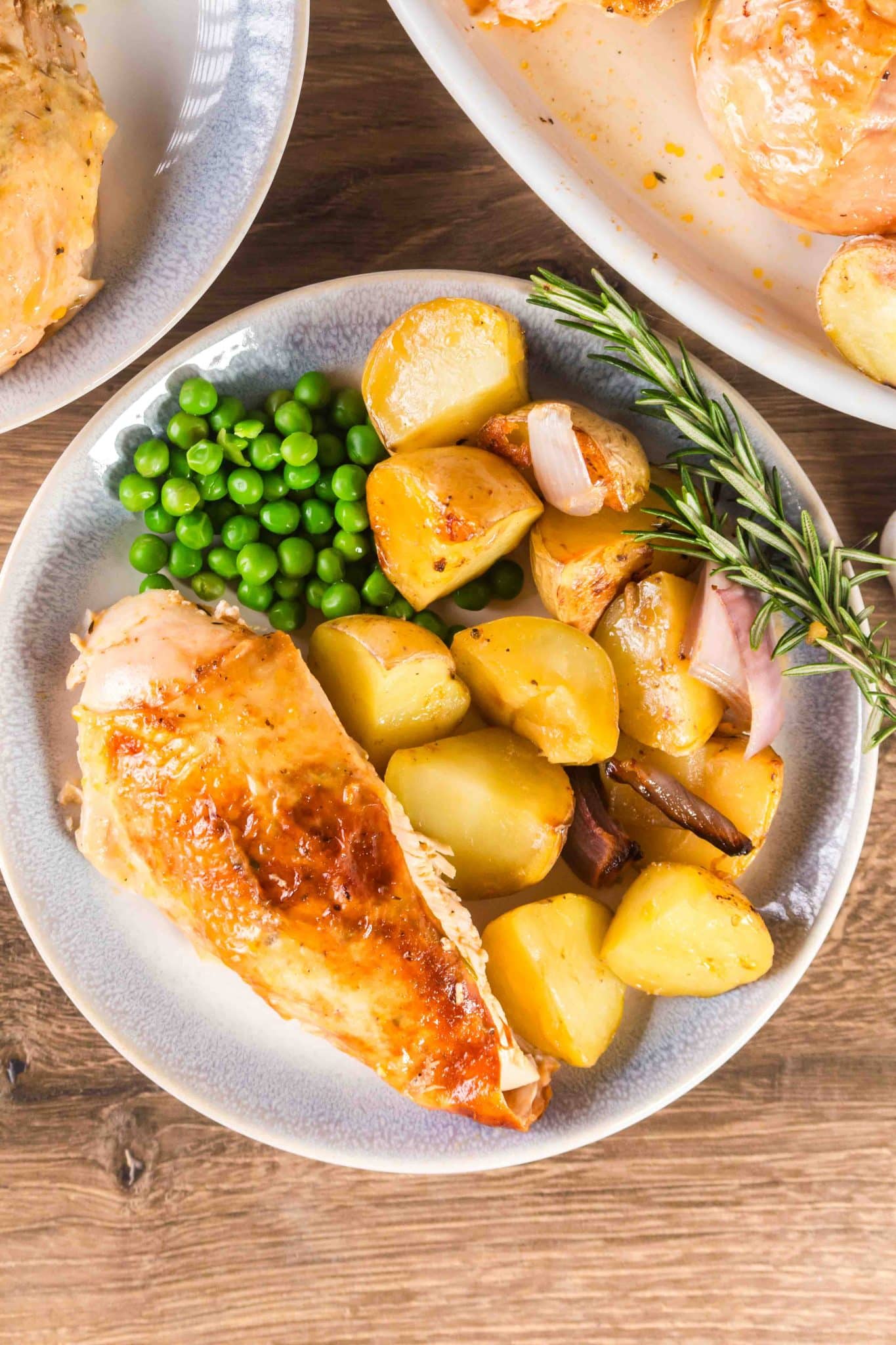 A piece of roasted chicken breast with the skin on, served on a plate with potatoes and peas.