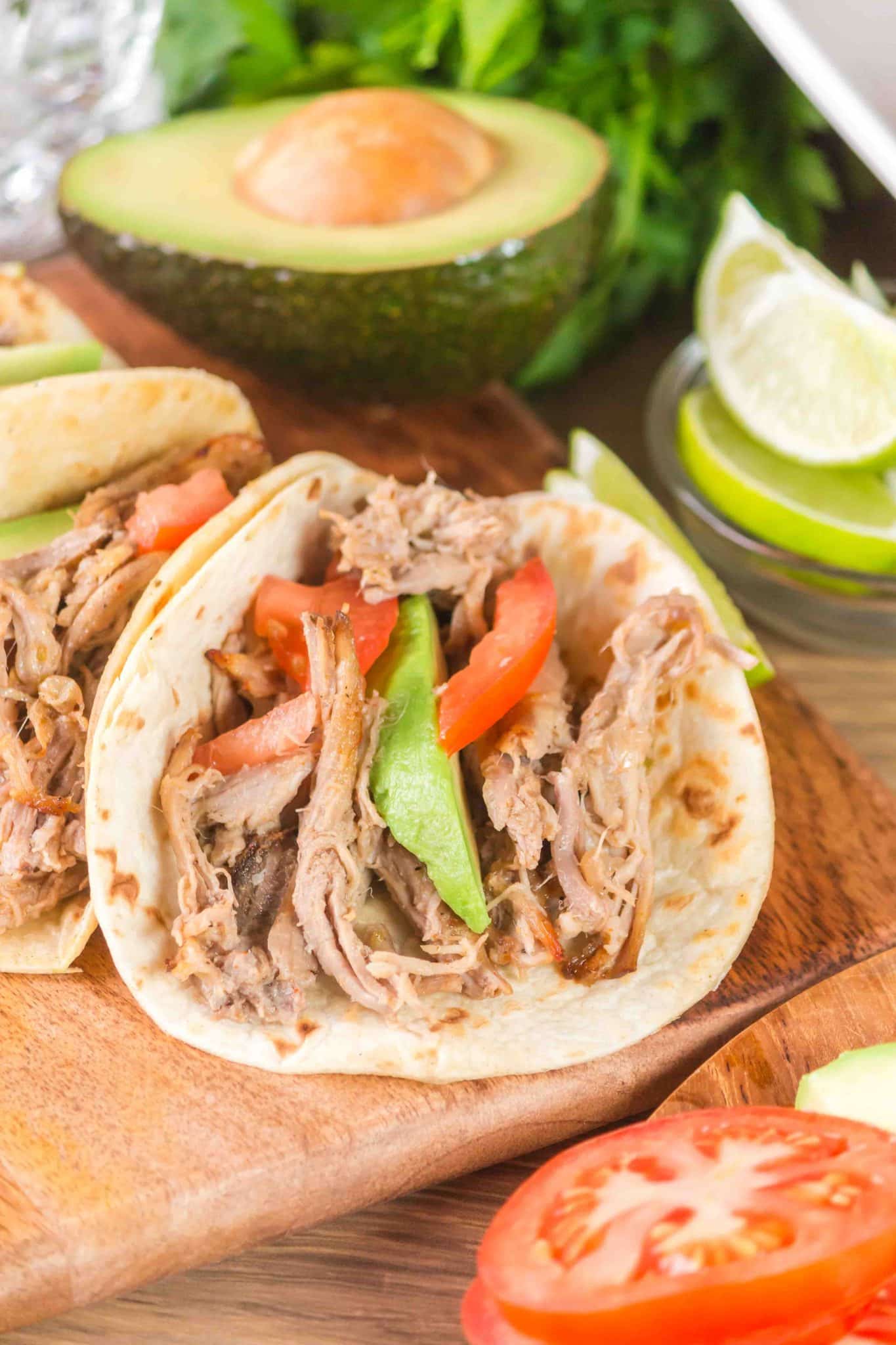 Angled view of a slow cooker pork carnitas taco garnished with tomatoes and avocado. Hostess At Heart