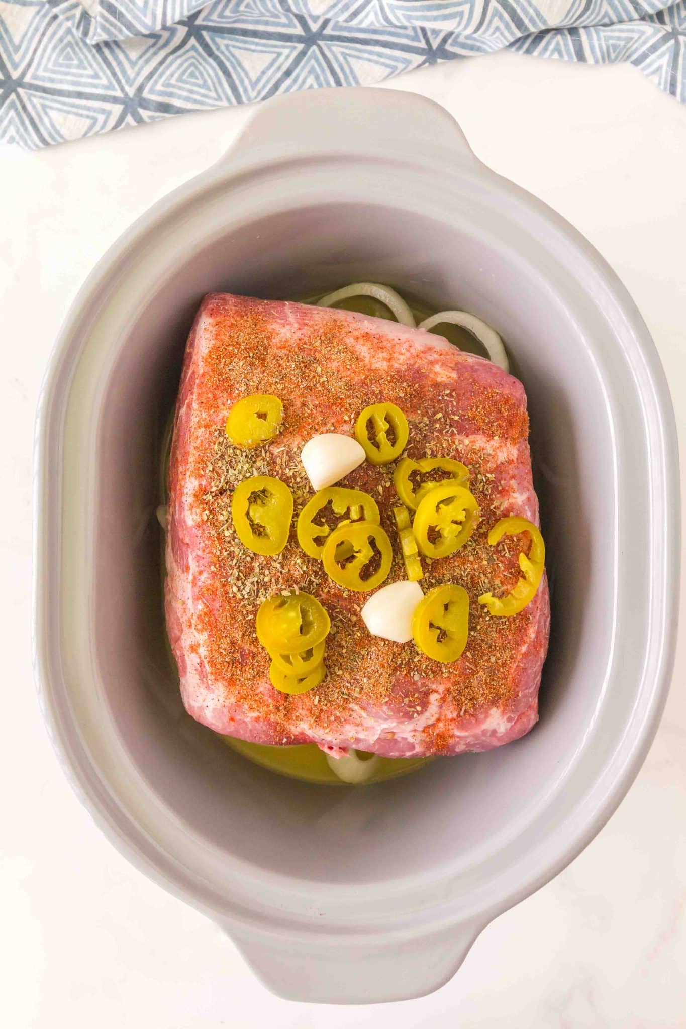 Top down view of a pork carnitas slow cooker recipe topped with spices, sliced jalapeno and garlic cloves Hostess At Heart