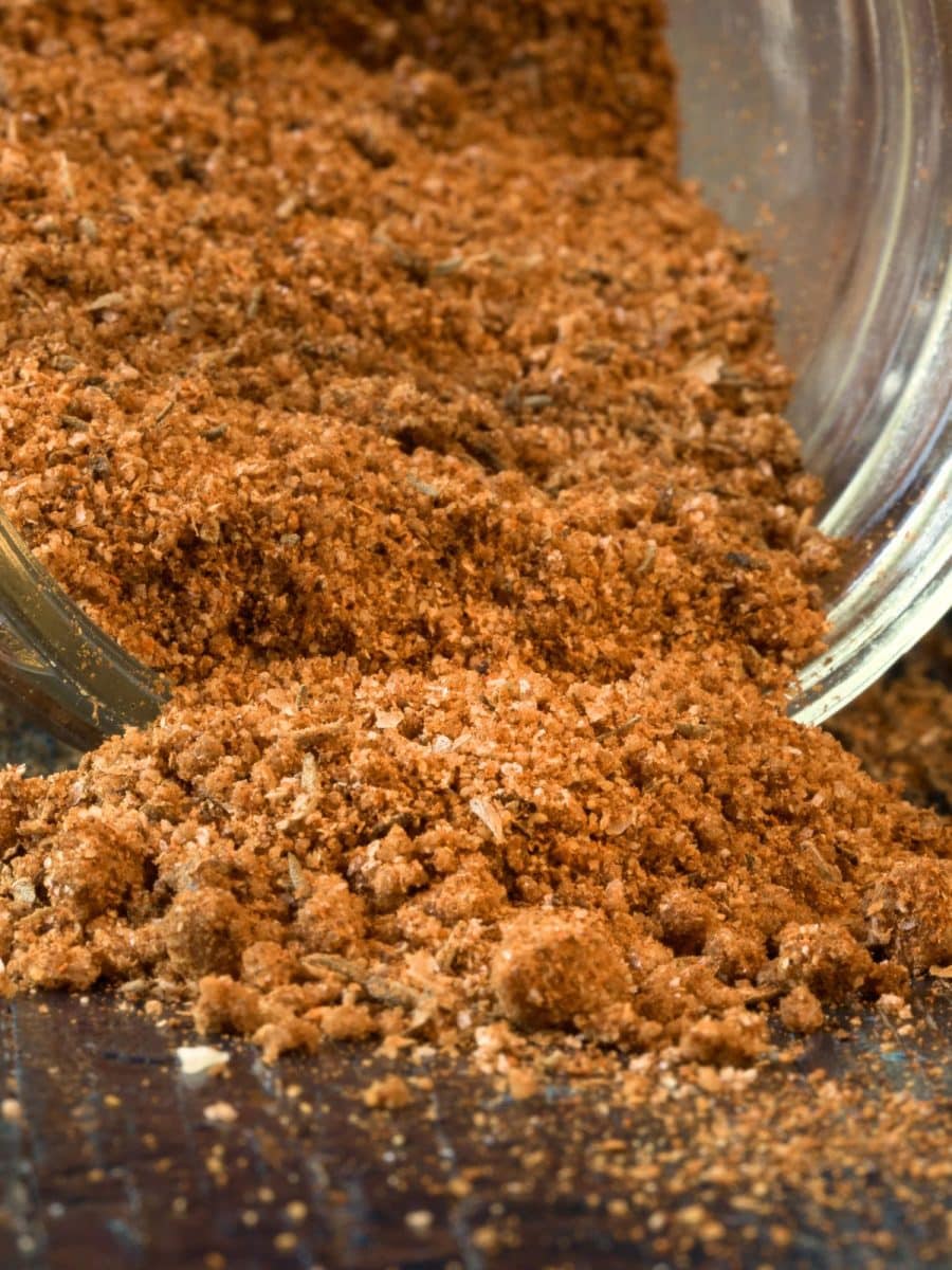 A spice jar tipped over with a creole spice blend pouring out of it. Hostess At Heart