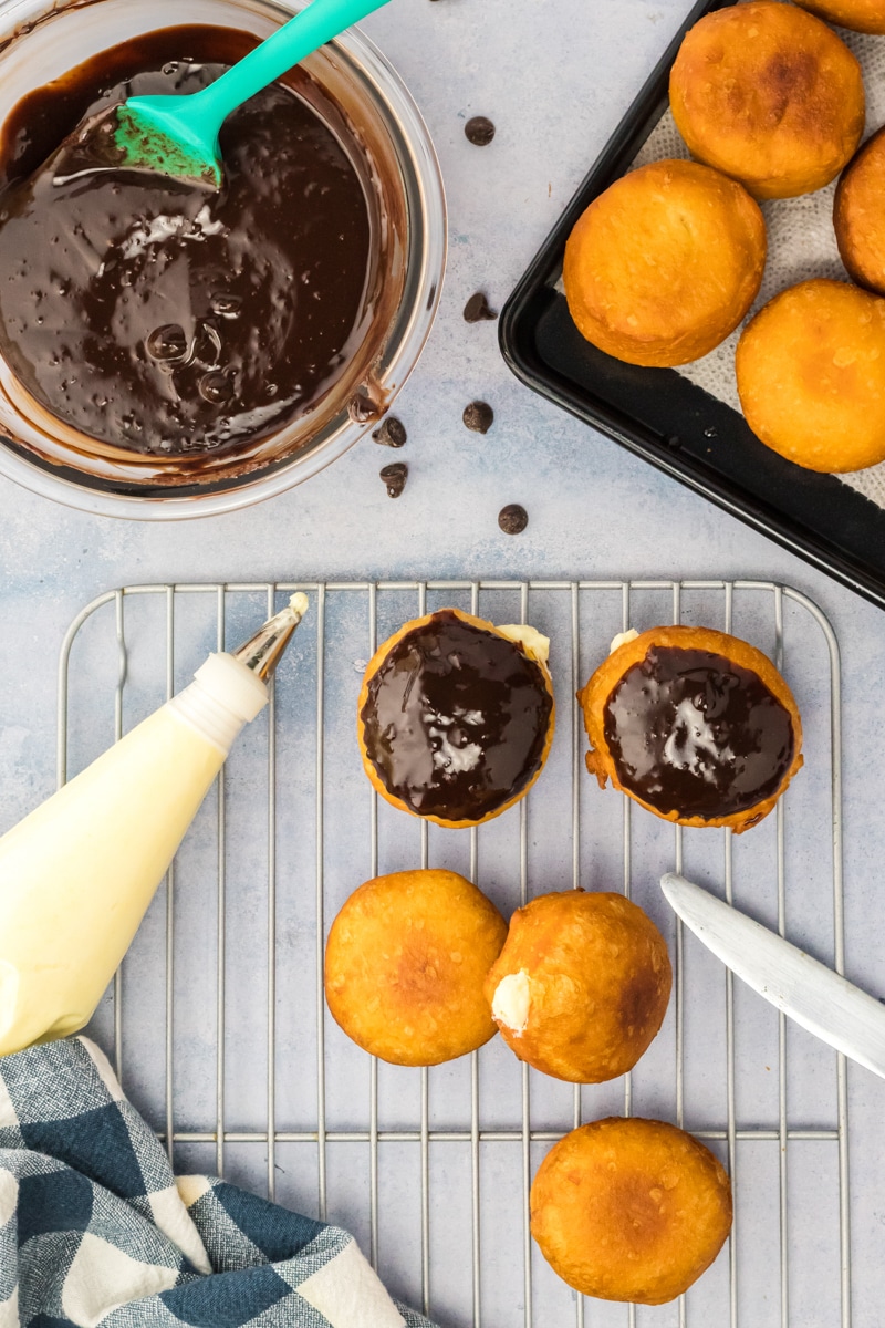 Top down image of semi-homemade cream filled doughnuts. Some are topped with a chocolate ganache while others have yet to be frosted. Hostess At Heart