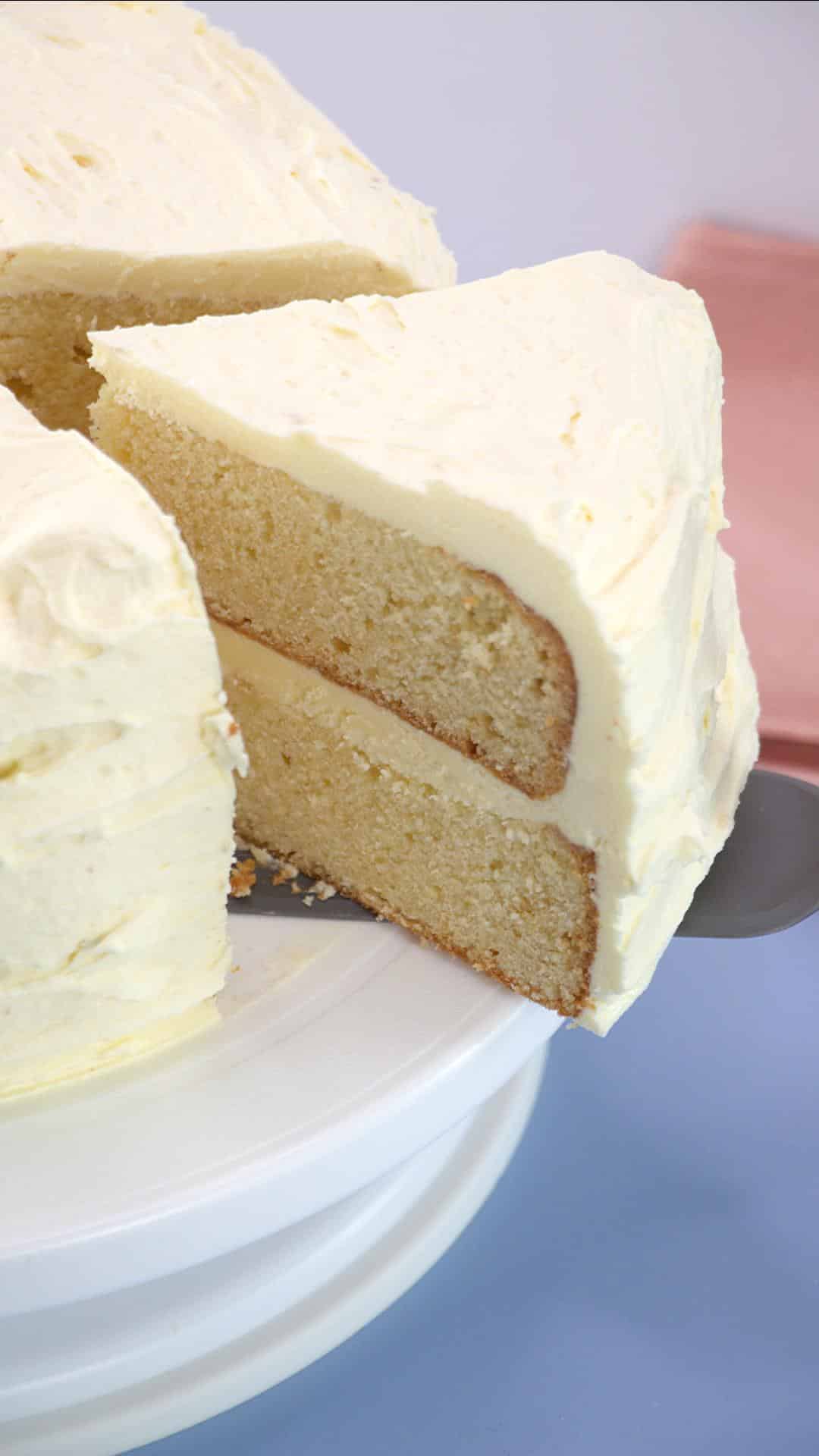 Sideview of a two-layer white two layer cake with a slice being removed using a cake server - Hostess At Heart