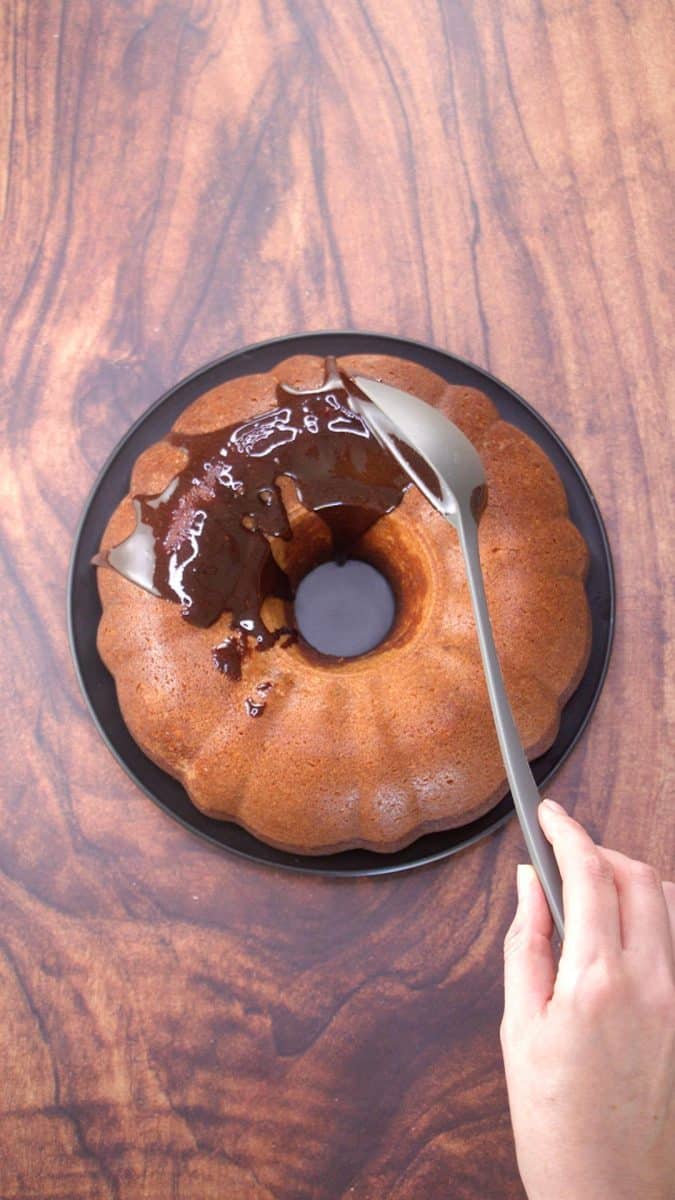 A spoon drizzling chocolate glaze over a bundt cake - Hostess At Heart
