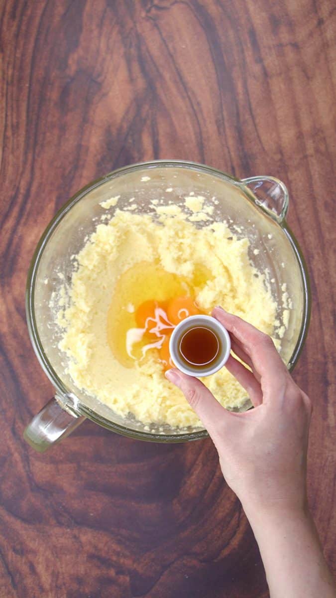 A mixing bowl filled with whipped butter and sugar topped with eggs. Vanilla is being added to the wet batter. Hostess At Heart