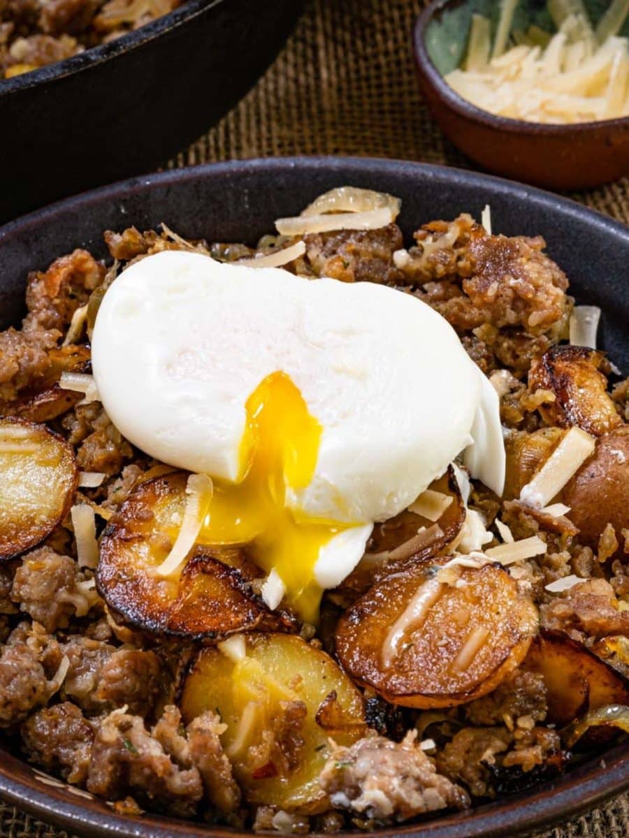 A bowl filled with skillet fried potatoes and sausage topped with a poached egg - Hostess At Heart