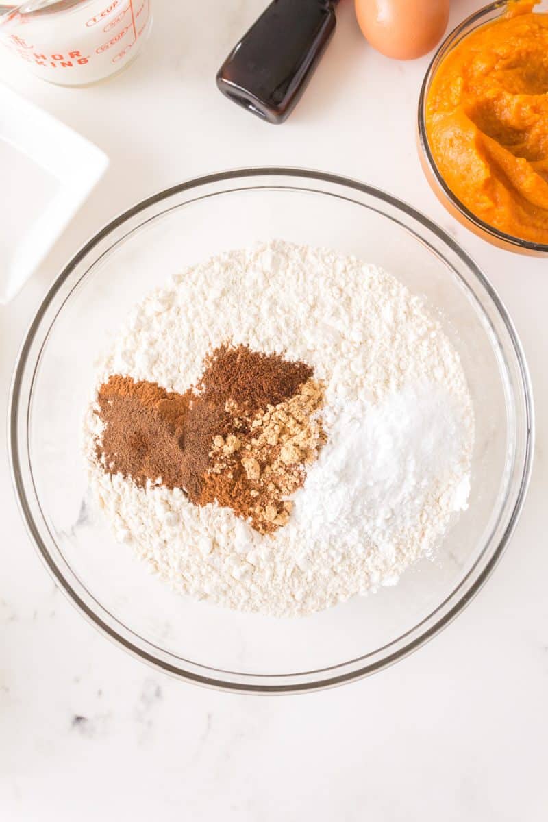 Dry ingredients used to make a Spiced Pumpkin Cake in a mixing bowl including flour, baking powder, baking soda, and spices. Hostess At Heart