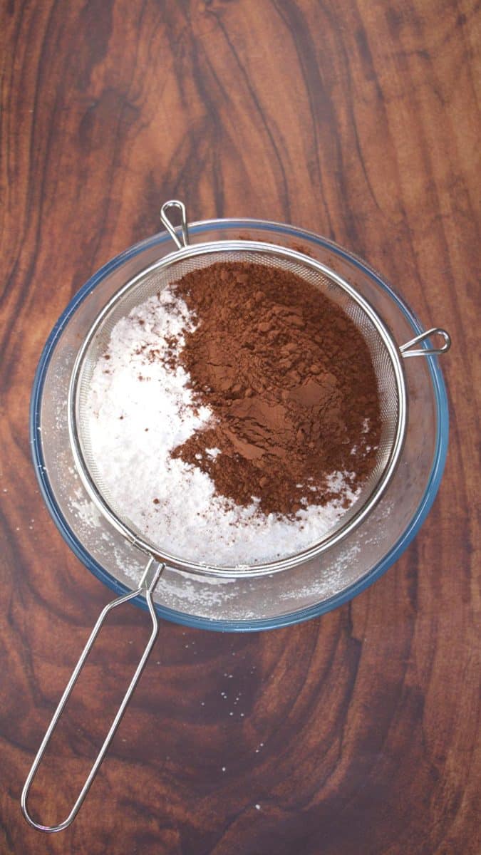 A fine mesh sieve holding powdered sugar and cocoa powder over a mixing bowl - Hostess At Heart