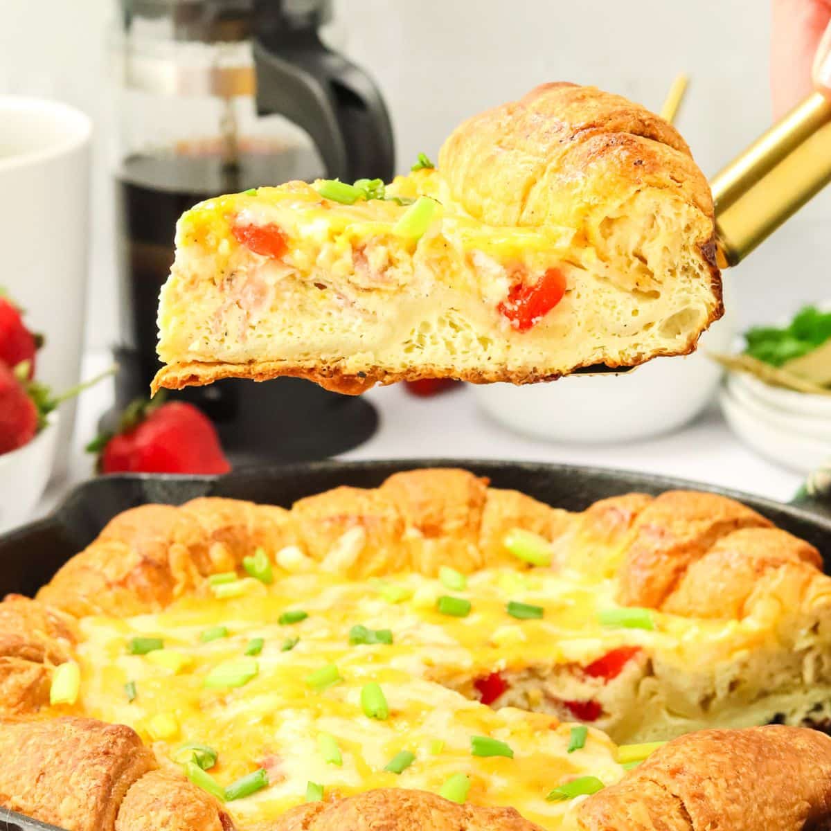 Sideview of a gold pie server topped with a slice of crescent breakfast casserole being lifted from a cast iron skillet. Hostess At Heart