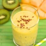 Angled view of a glass filled with a mango kiwi smoothie topped with flax seed. Hostess At Heart