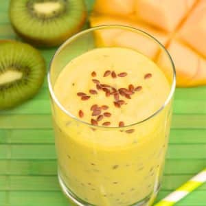 Angled view of a glass filled with a mango kiwi smoothie topped with flax seed. Hostess At Heart