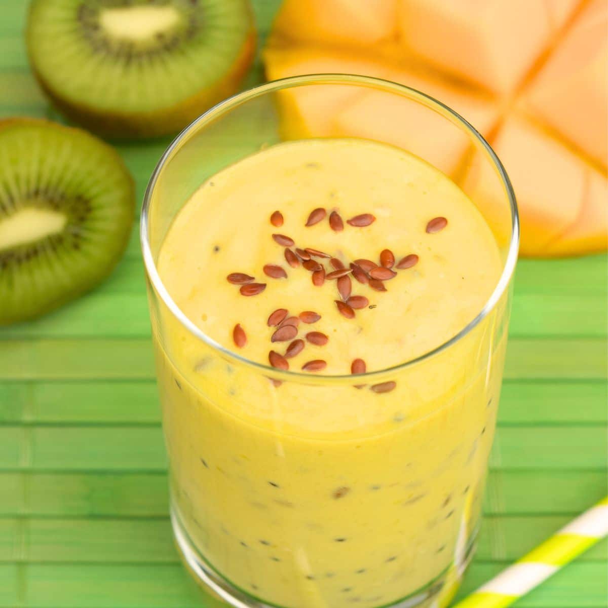 Angled view of a glass filled with a mango kiwi smoothie topped with flax seed. Hostess At Heart