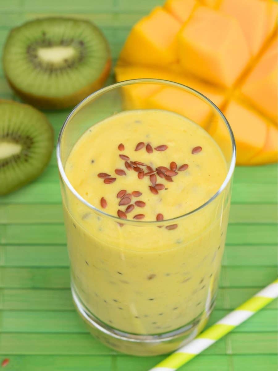 Angled view of a glass filled with a mango kiwi smoothie topped with flax seed. Hostess At Heart
