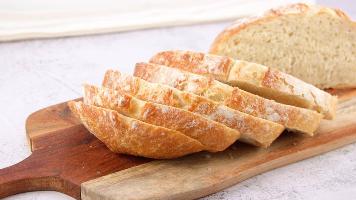 Tableview of a round loaf of almost no-knead bread with the front slices fanned in front of it sitting on a cutting board. Hostess At Heart