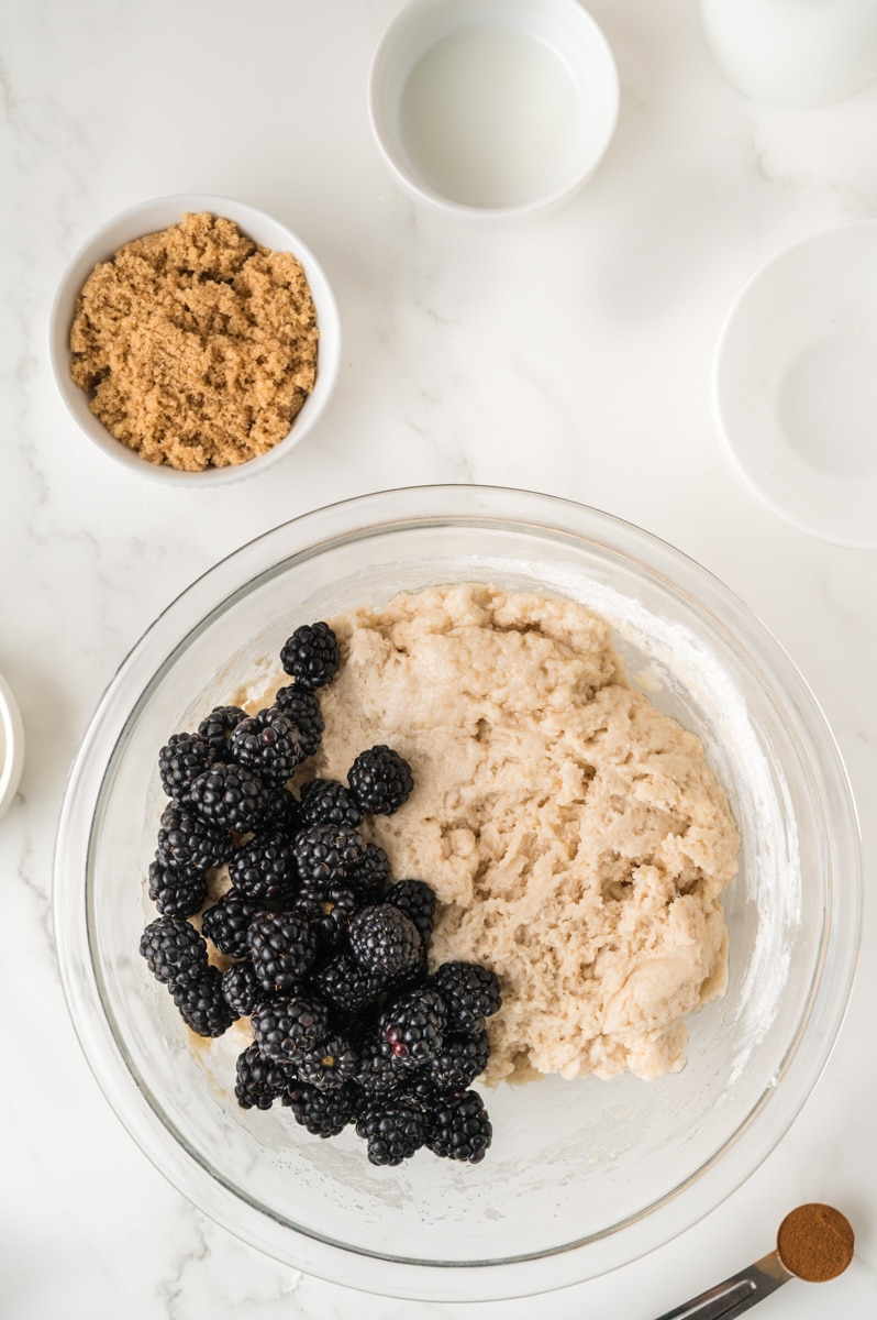 Thick muffin batter with blackberries on the side of the bowl.