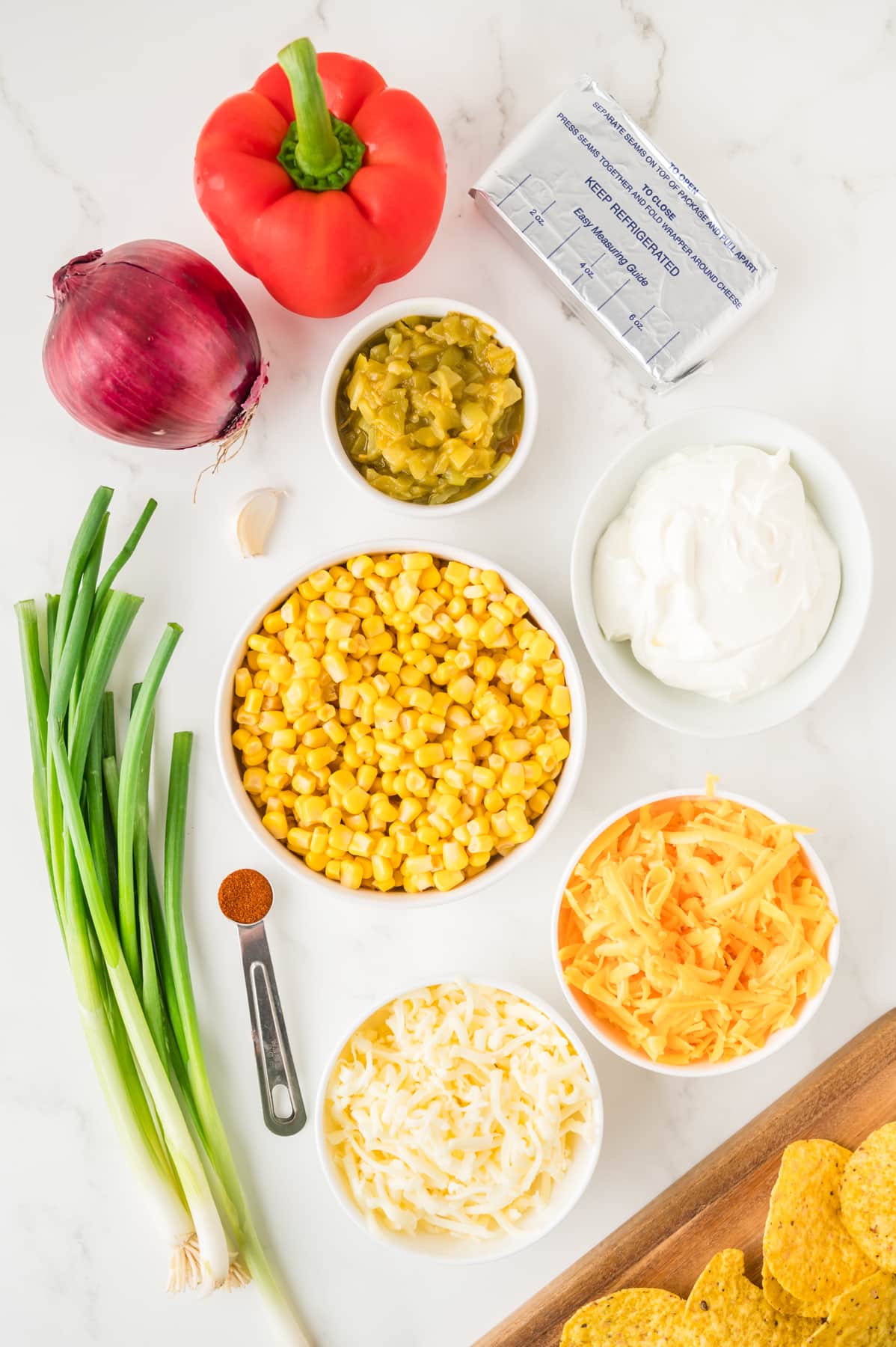 Recipe ingredients for hot cheesy corn dip including: cream cheese, sour cream, monterey jack cheese, cheddar cheese, green onions, green chilies, red pepper, garlic and paprika. Hostess At Heart