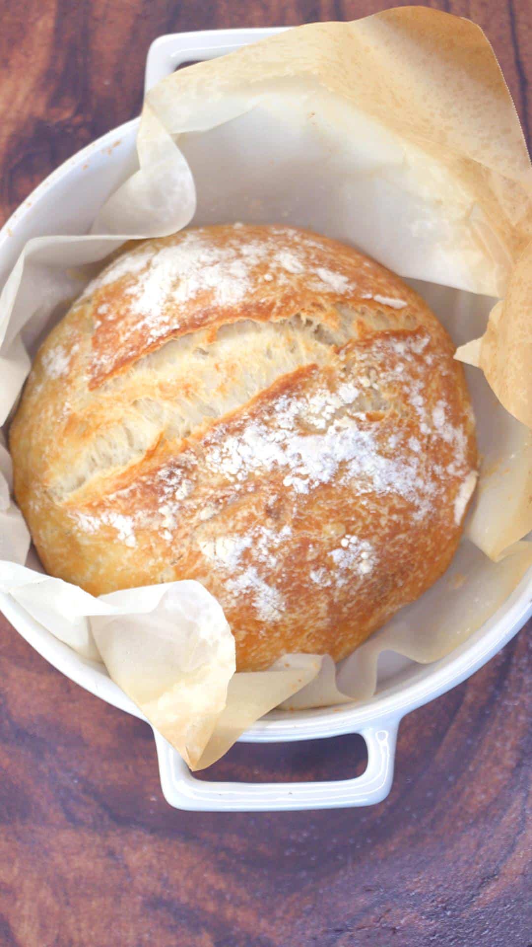 A homemade baked round bread boule sitting on parchment paper in a dutch oven. Hostess At Heart