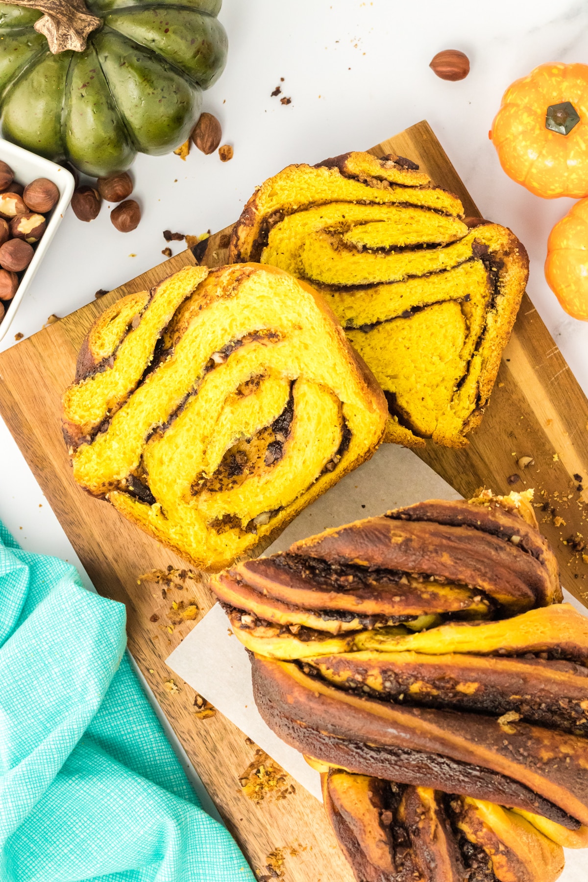 Top down view of a loaf of twisted chocolate pumpkin bread dotted with crushed hazelnuts. The front of the loaf is slices showing a top down view of the swirls. Hostess At Heart