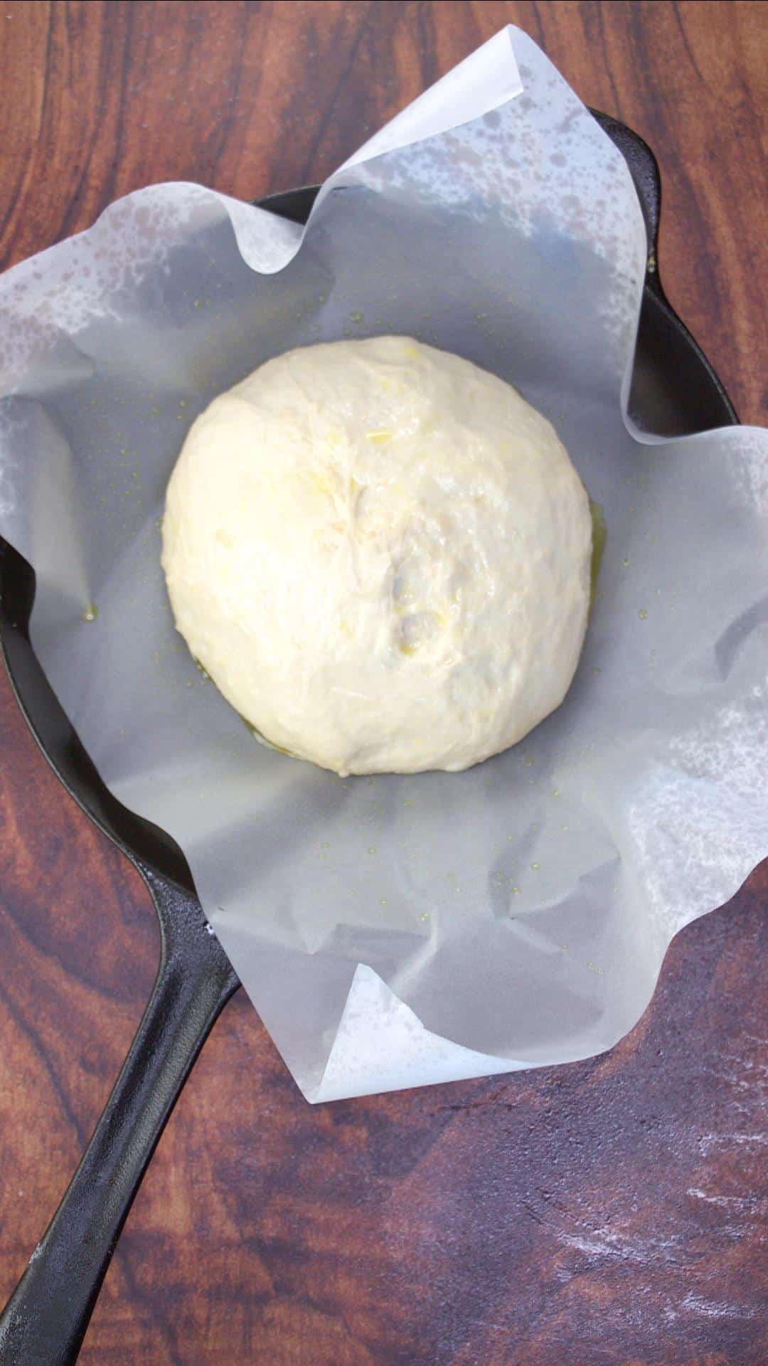 Round shaped bread dough sitting on a parchment paper-lined skillet. Hostess At Heart