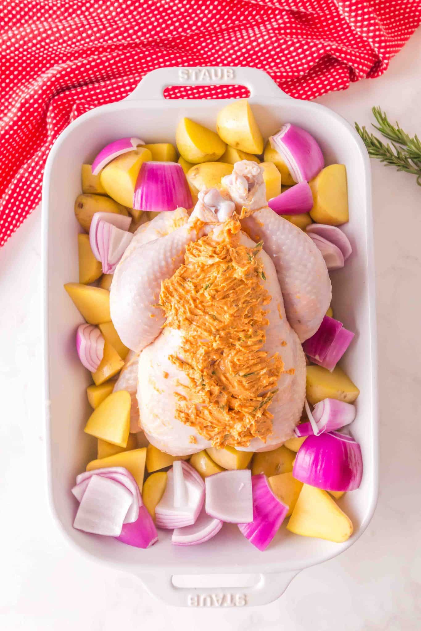whole raw chicken with potatoes and onions around the base, and compound butter both inside the skin and outside the skin on top of the chicken.