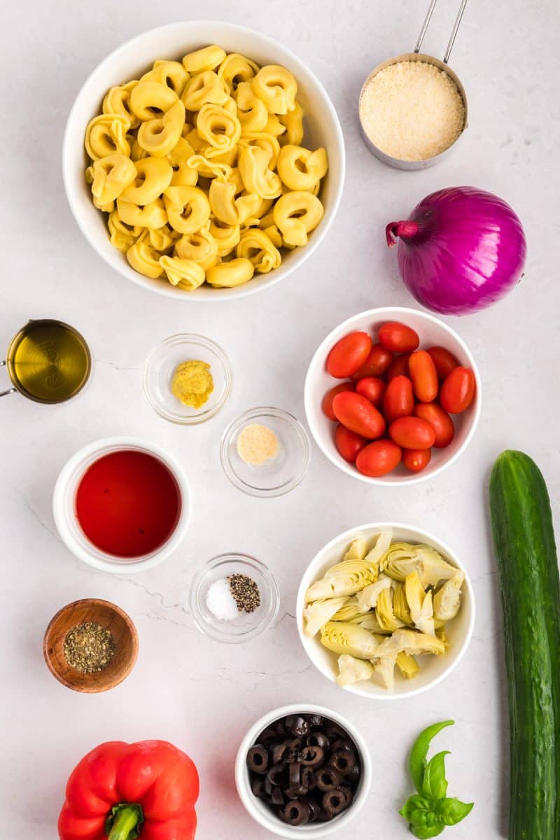 Tortellini Pasta Salad recipe ingredients including cooked cheese tortellini, red pepper, artichokes, tomatoes, onions, cucumbers, and vinaigrette. Hostess At Heart