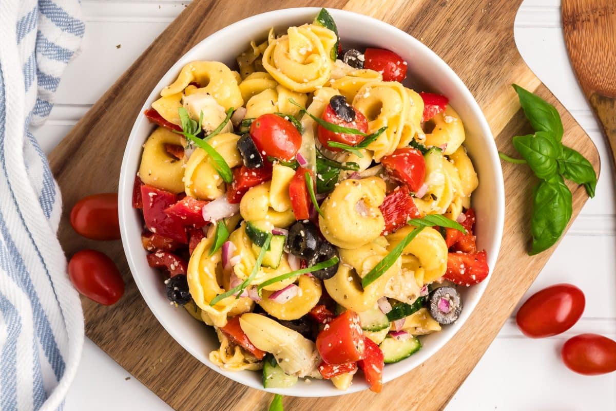 A top down view of a Tortellini Pasta Salad filled with tomatoes, artichokes, sliced olives and fresh basil. Hostess At Heart