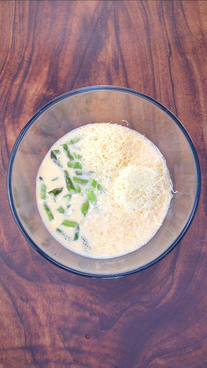 A mixing bowl filled with milk, beaten eggs, shredded cheese, fresh and asparagus - Hostess At Heart