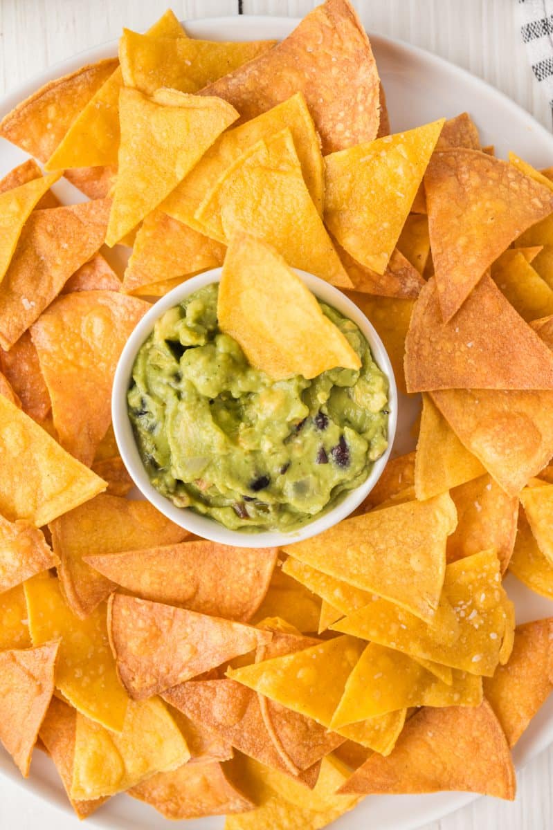 Closeup view of a platter with a bowl of guacamole surrounded by homemade corn tortilla chips - Hostess At Heart