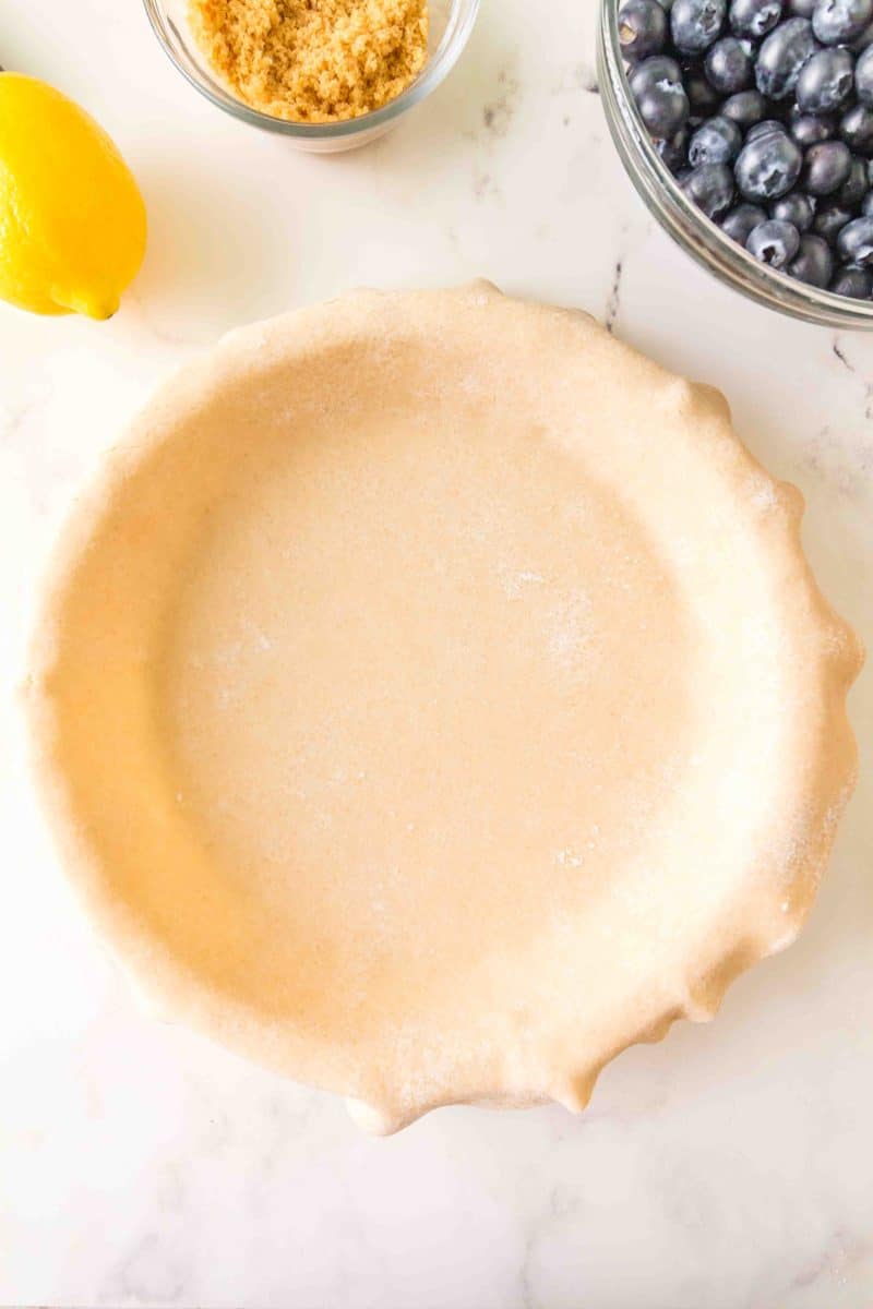 Top down view of rolled pie dough draped over a pie plate - Hostess At Heart
