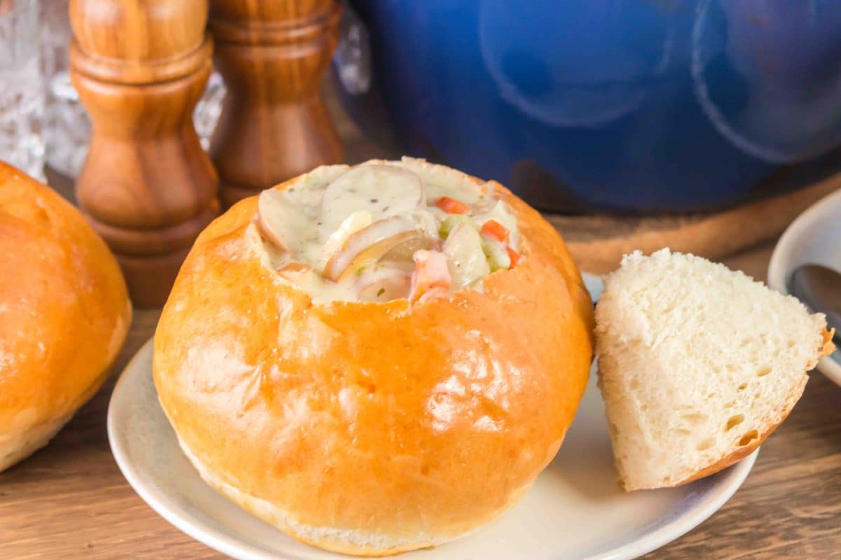 A bread bowl filled with clam chowder soup. The wedge removed from th boule is propped up to the side - Hostess At Heart