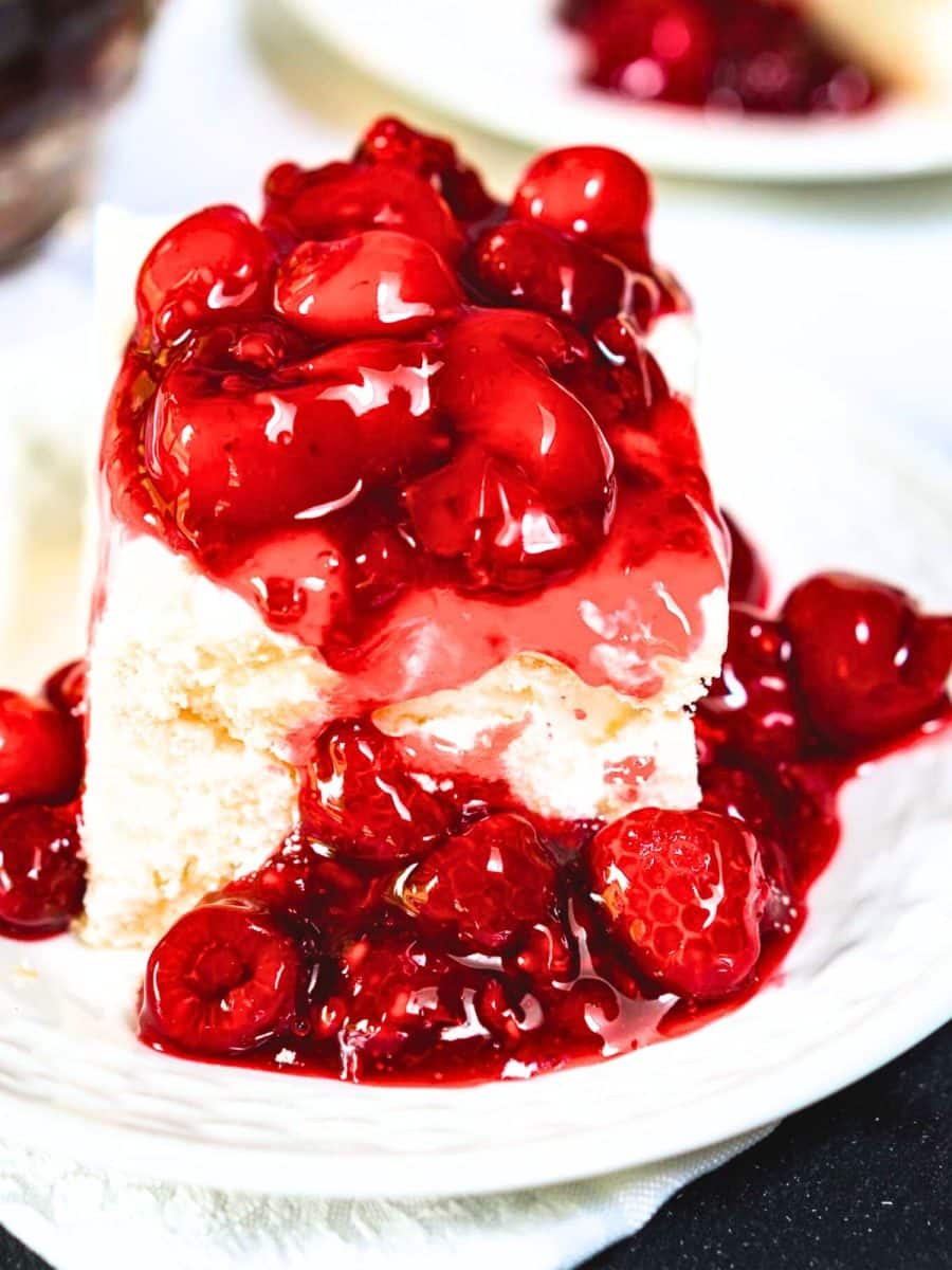 Angled view of a plate containing a bar of baked meringue topped with sweet cream cheese and a thick raspberry cherry sauce - Hostess At Heart