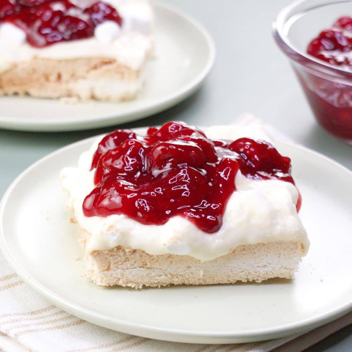 Angled view of a baked meringue dessert topped with a cream cheese filling and cherry raspberry topping. Hostess At Heart
