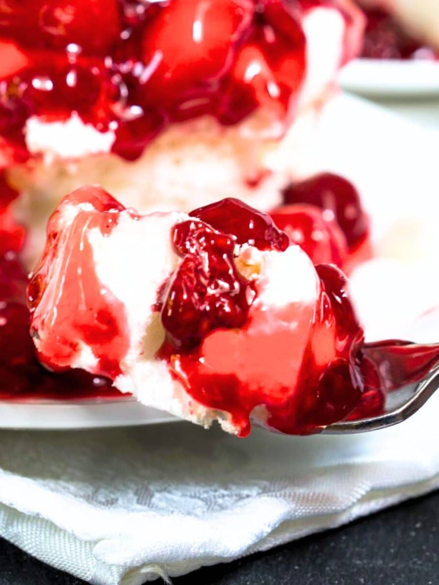 A fork filled with a meringue cream cheese dessert with a cherry raspberry sauce. Hostess At Heart