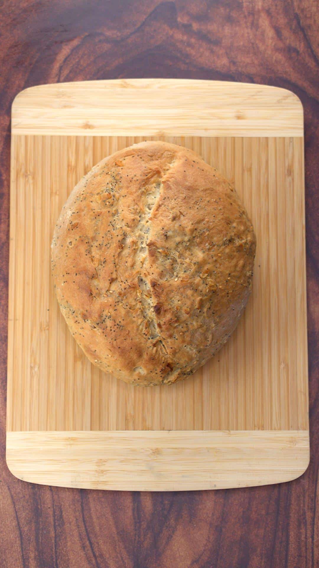 Top down view of a baked loaf of Pumpernickel Bread on a bread board - Hostess At Heart