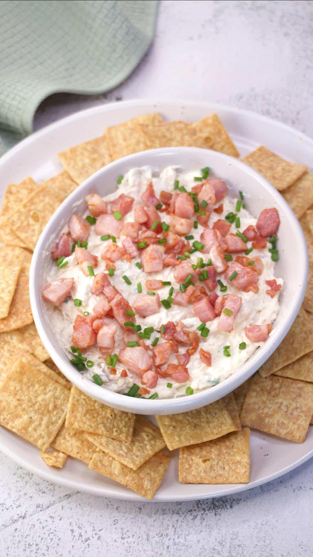 Top down view of a serving bowl filled with cold crab and bacon dip topped with fresh chives and surrounded with wheat crackers - Hostess At Heart