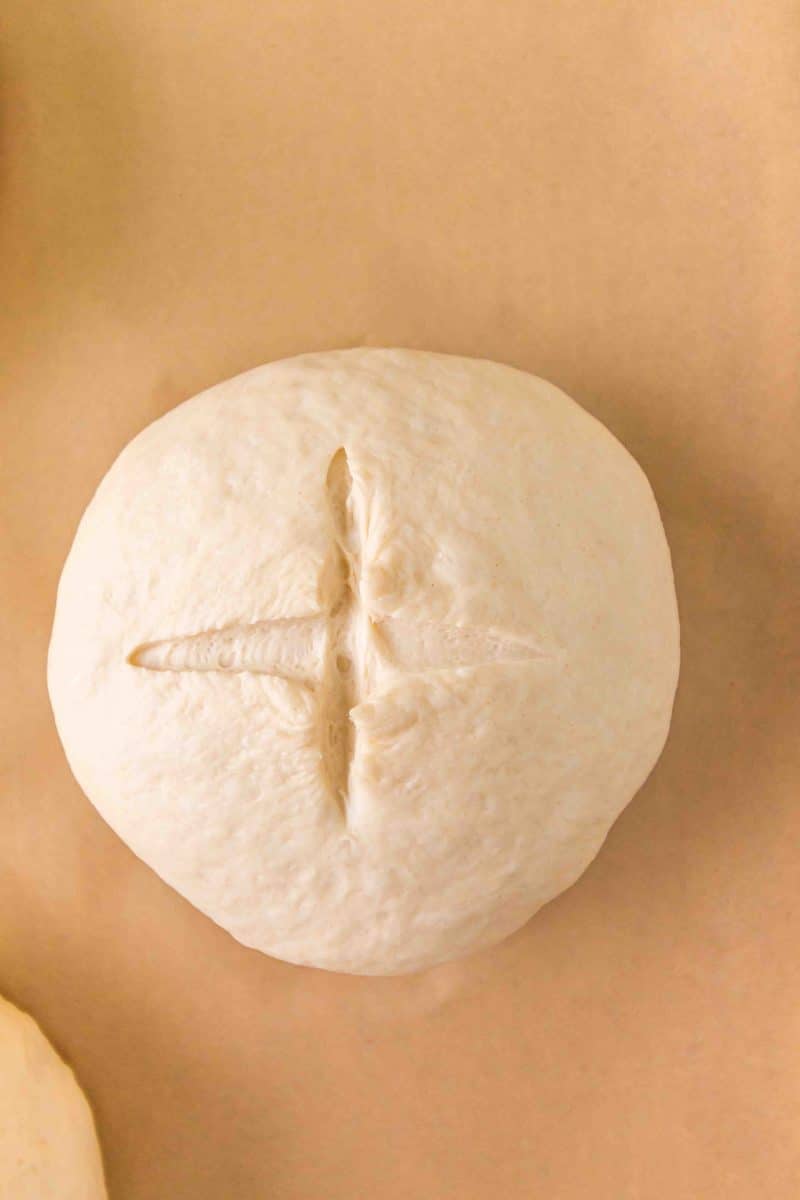 Top down view of a homemade roll of dough with an x scored into the top. Hostess At Heart