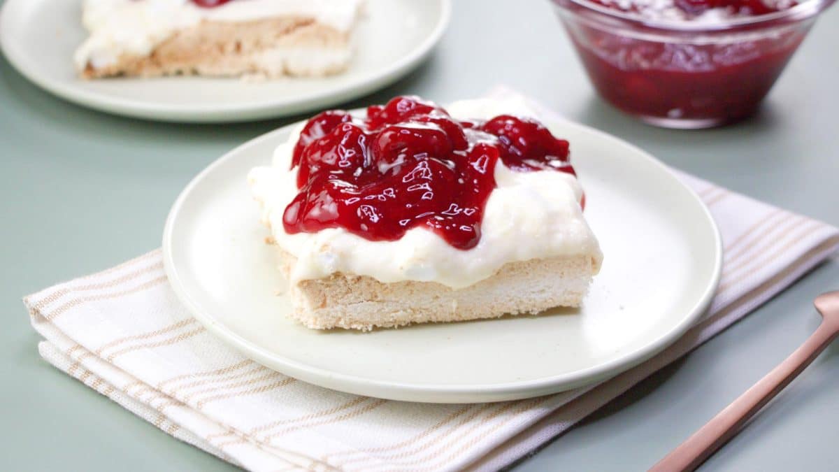 A sideview of an egg white meringue bar with a layer of sweet cream cheese topped with a beautiful cherry sauce - Hostess At Heart