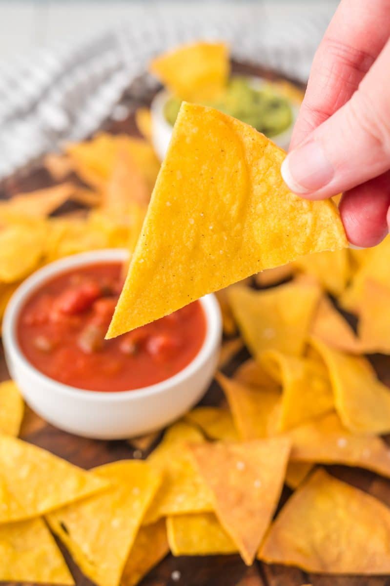 A closeup of a hand holding a freshly baked corn tortilla chip - Hostess At Heart
