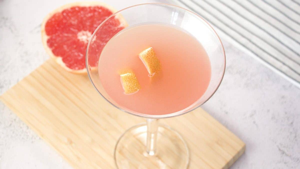 Top angled view of a grapefruit martini cocktail garnished with rind sitting next to a pink grapefruit half - Hostess At Heart