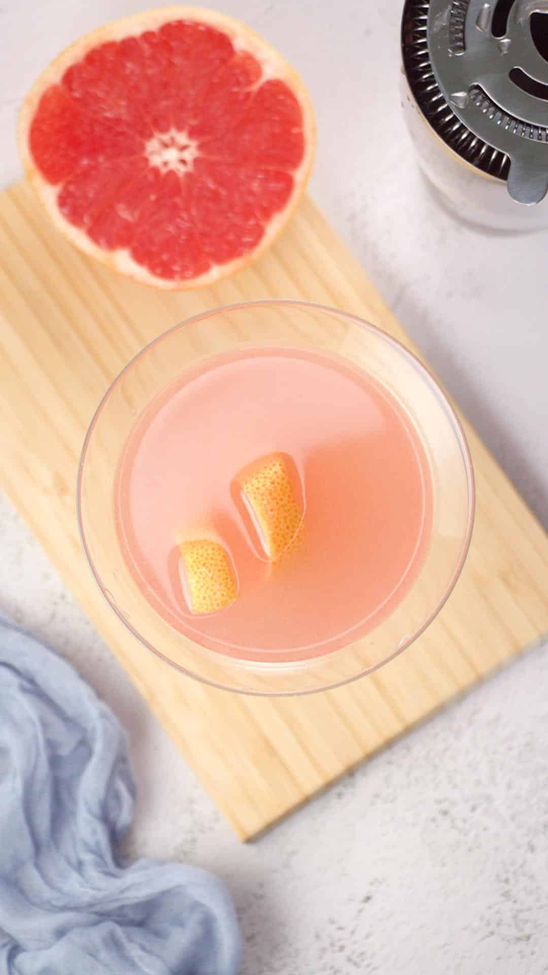 Top down view of a red grapefruit martini garnished with a a strip of the peel - Hostess At Heart