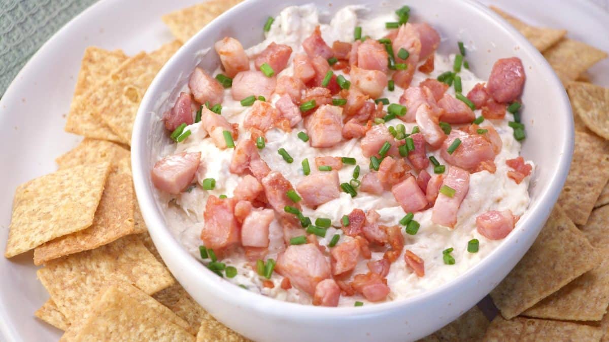 Angled view of a bowl of cold crab dip topped with cooked bacon. Hostess At Heart