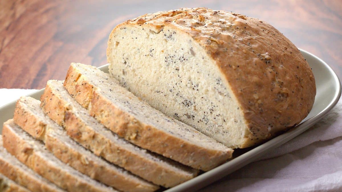A sideview of a baked loaf of simple pumpernickel bread partially sliced - Hostess At Heart