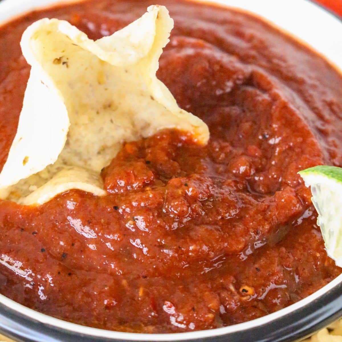 A bowl of deep read rojo salsa with a tortilla chip dipped into the side. - Hostess At Heart